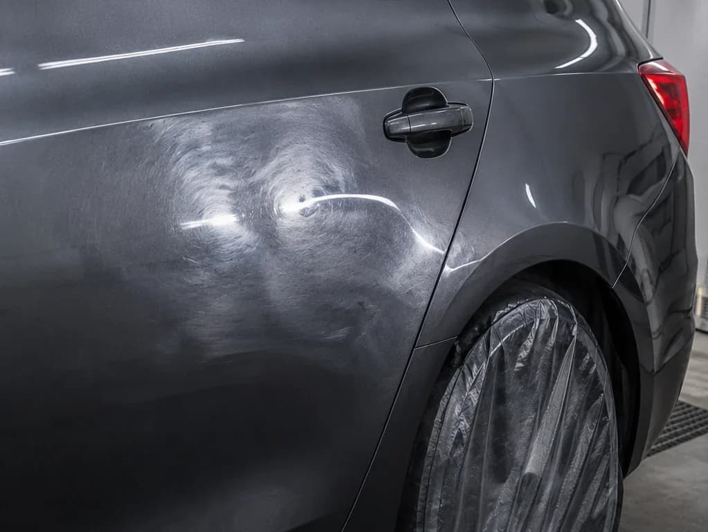 Rear door and quarter before repair: failed refinish, sand scratches, and poor blend under raking light